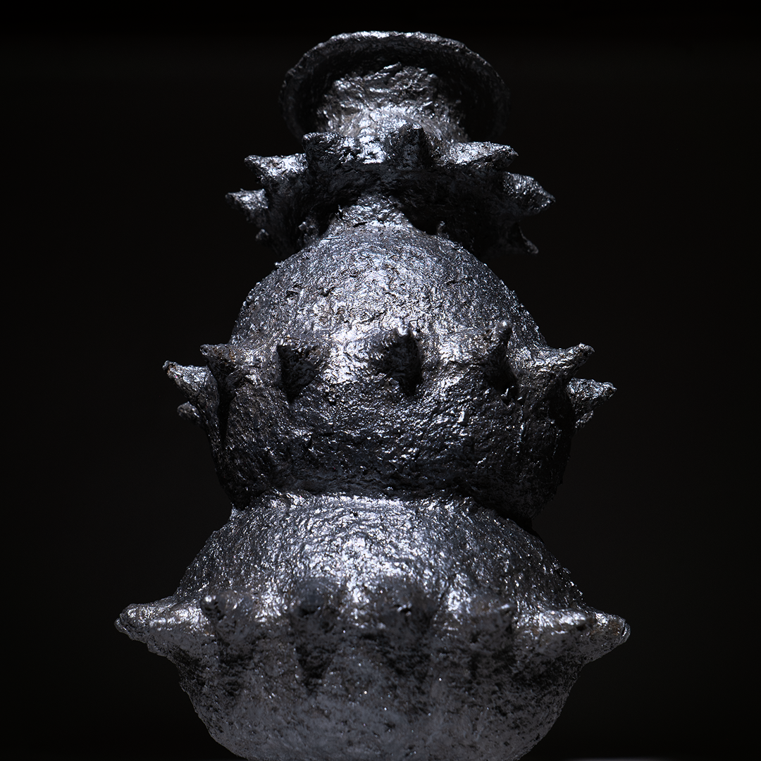 Handbuilt papier-mâché sculptural vessel “Tálä” by Pulp Fictitious, showing its stacked, spiked silver forms against a dark background.