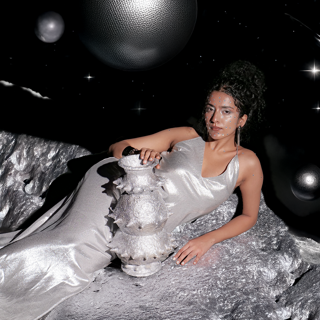 Person posed in a cosmic setting with the handbuilt papier-mâché sculptural vessel “Tálä” by Pulp Fictitious, finished in silver.